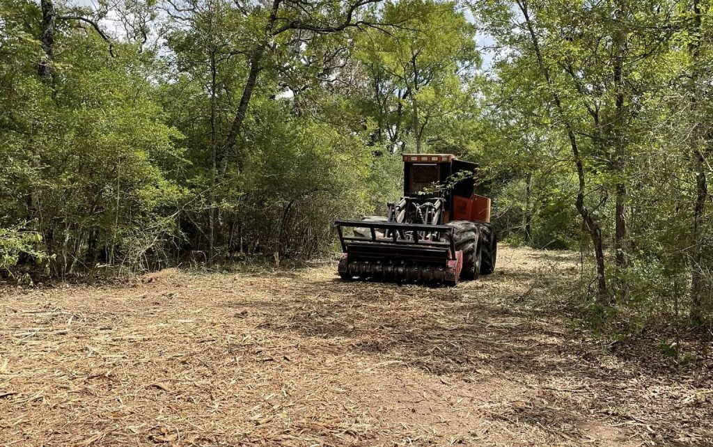 Forestry mulching machine clearing brush and trees in wooded area